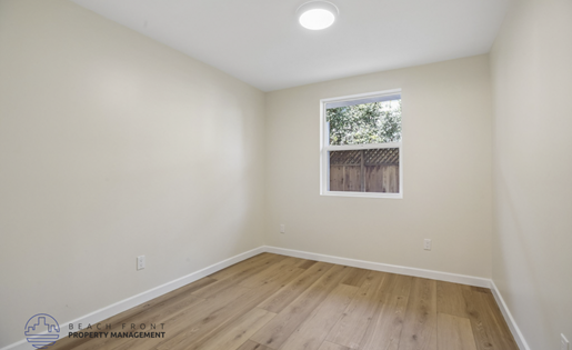 A room with wooden floors and a window showing a fence and trees outside.